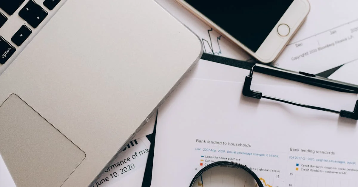 A detailed view of a workspace with laptop, smartphone, documents, and magnifying glass for financial analysis.