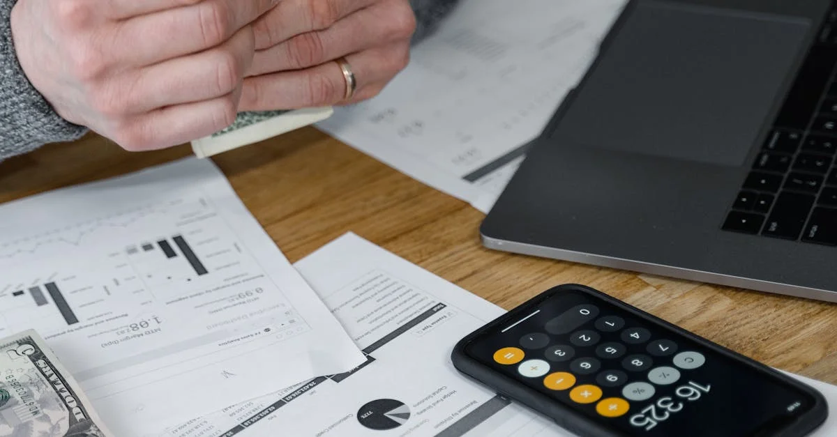 Hands counting money at a workspace with a laptop, calculator, and financial documents.