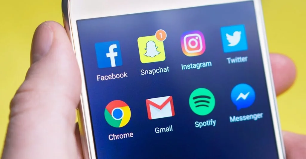 A person's hand holding a smartphone displaying social media and communication apps.