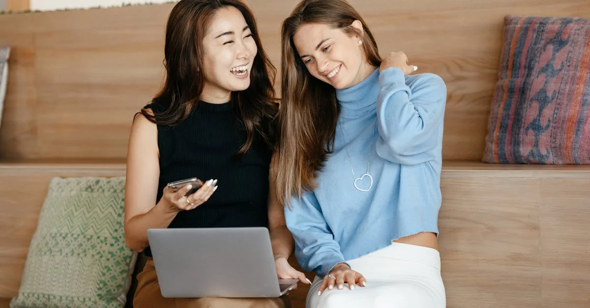 Cheerful young multiracial friends smiling and surfing internet on netbook while using mobile phone