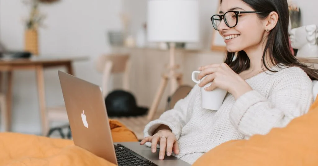 Woman enjoying a cozy moment with a laptop and coffee in a modern interior setting.